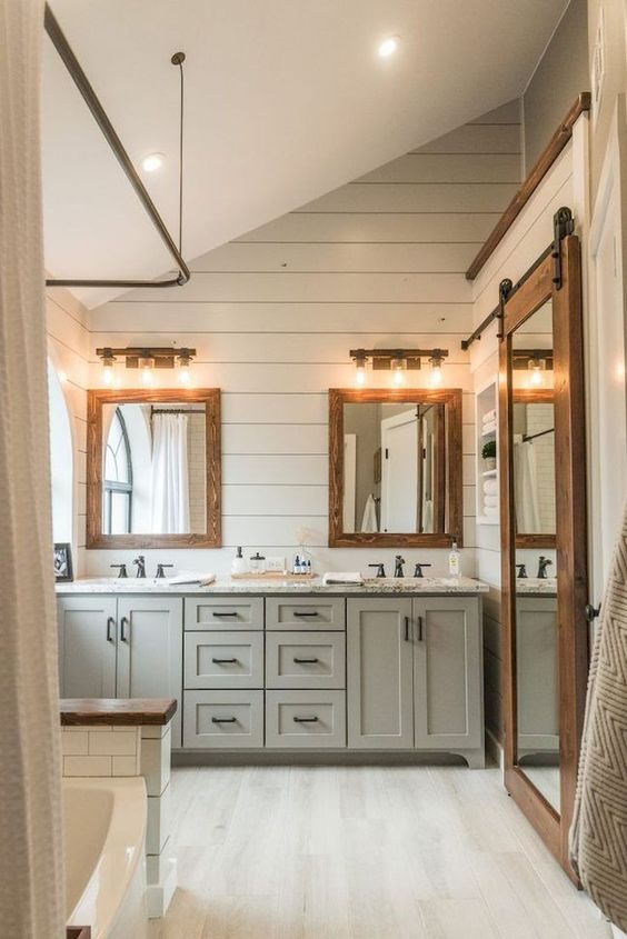 a modern farmhouse bathroom with light-colored vanities, wooden frame mirrors and whitewashed floors and walls