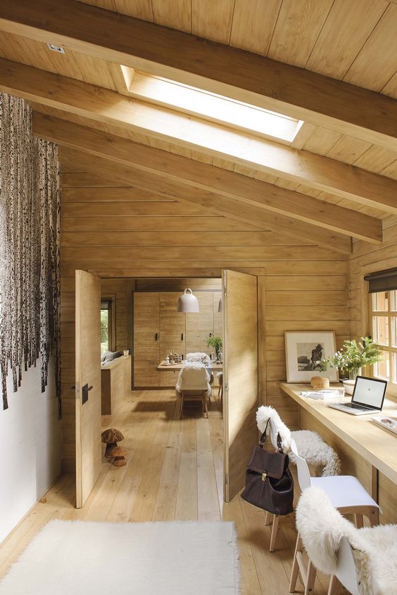 a modern rustic home office with a shared desk, a couple of chairs, an attic ceiling with a skylight and soem faux fur