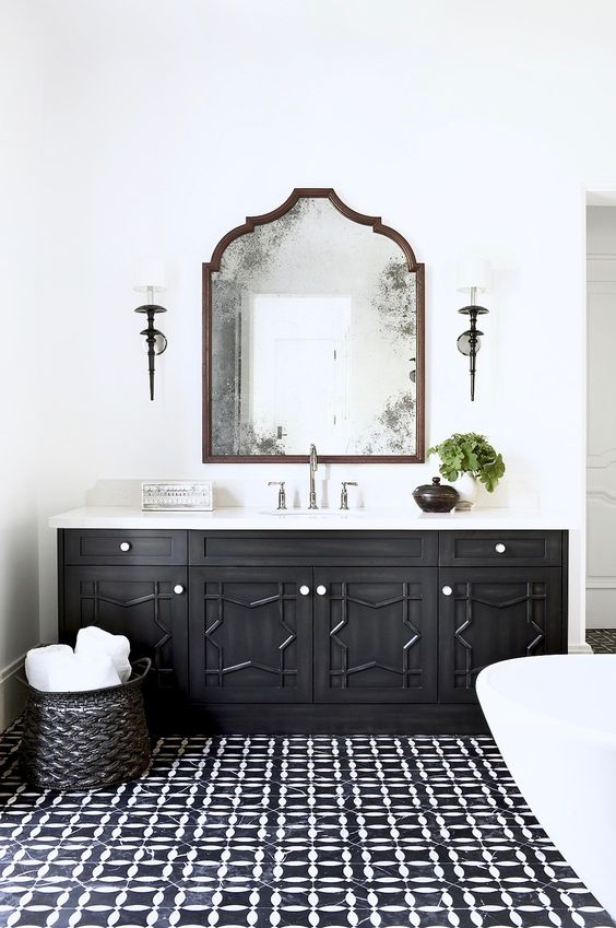 a monochromatic Moroccan bathroom with a carved wooden vanity, a tiled floor and a mirror with a catchy shape