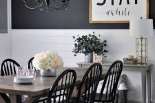 a monochromatic farmhouse dining room with a black and white wall, a large sign, a stained table and black chairs