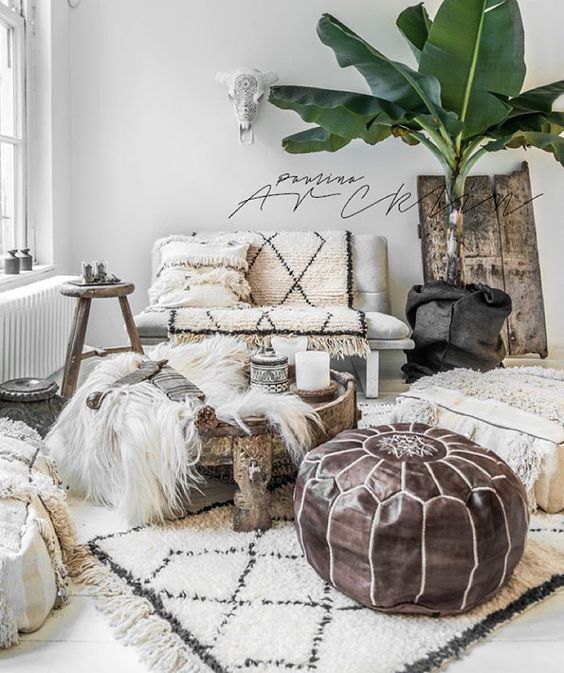 a neutral Moroccan living room with lots of patterned textiles, a leather ottoman and a potted palm