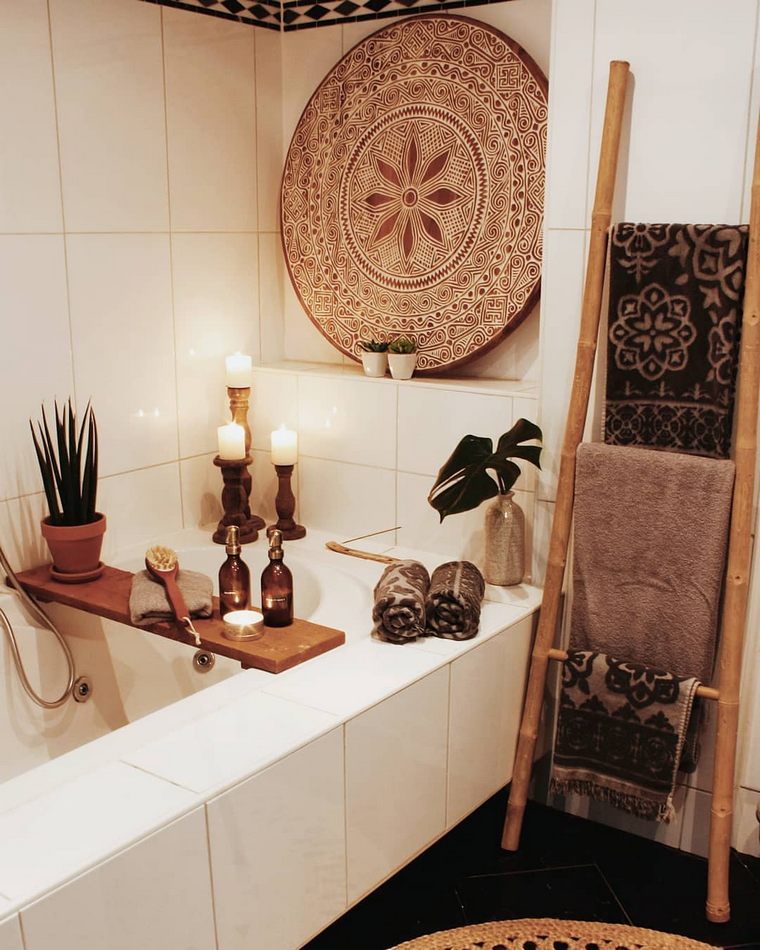 a neutral bathroom with a decorative tray, potted greenery and candles, a ladder with printed towels and a jute rug