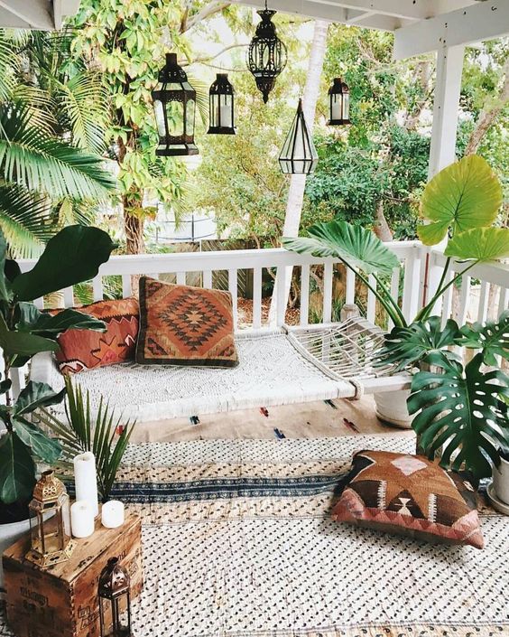 a neutral boho patio with a woven hammock, printed rugs, pillows, candles and lanterns hanging over the space