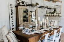 a neutral farmhouse dining room with a shabby chic buffet, a dark-stained table, white metal chairs, a ladder with crystal chandeliers