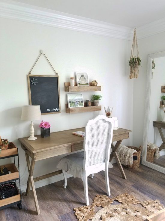 a neutral farmhouse home office with a wooden trestle desk, a white chair, a jute rug and wooden shelves