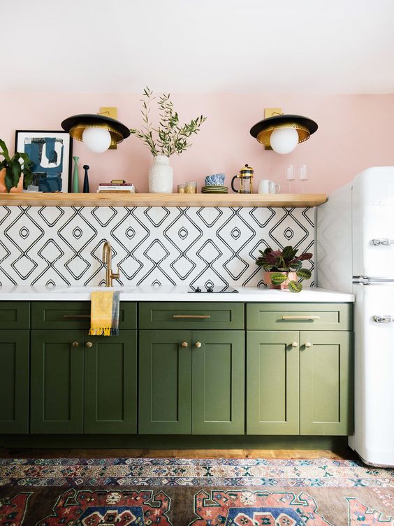 a pink wall, a geometric tile backsplash, green cabinets and a colorful boho rug