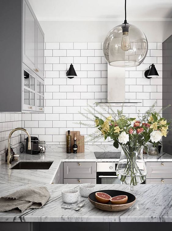 a retro-inspired Nordic kitchen with white tiles, stone countertops, grey cabinets and pendant lamps