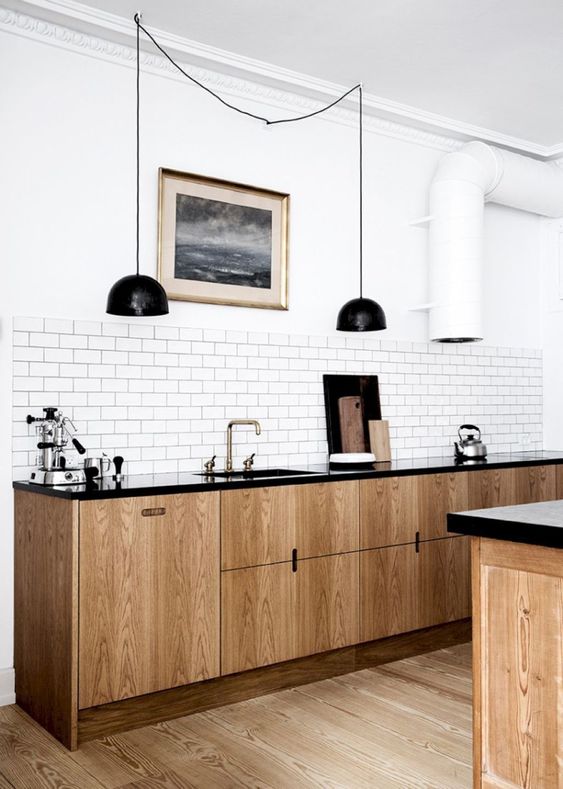 a retro-inspired Scandinavian kitchen with light wood cabinets, black countertops, black pendant lamps, a white tile backsplash