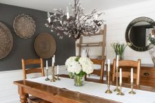 a rustic dining room with planked walls, a gallery wlal of baskets, a stained table and chairs, a white bench and a catchy chandelier