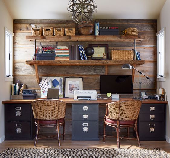 a rustic home office with a salvaged wooden wall, a shared desk, woven chairs and an open shelving unit