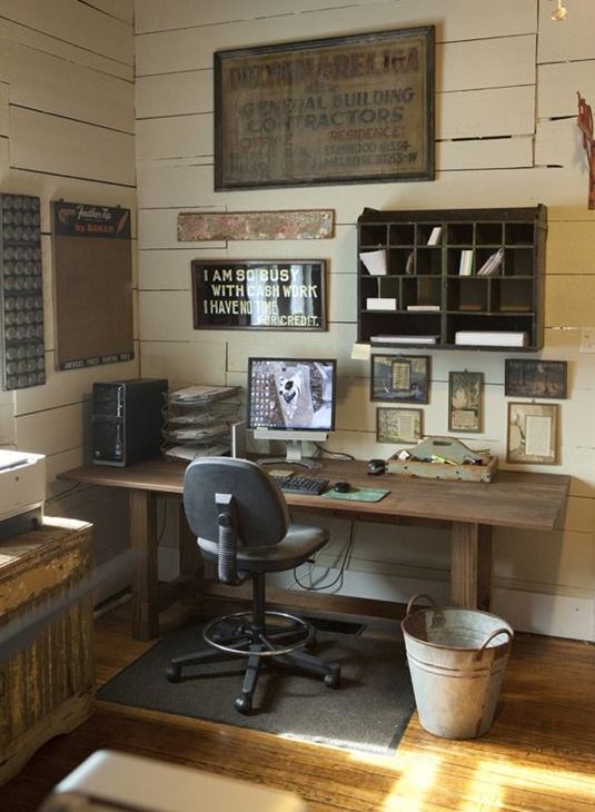 a rustic industrial home office with beadboards, a wooden desk, a shabby cabinet, a modern chair and a bucket