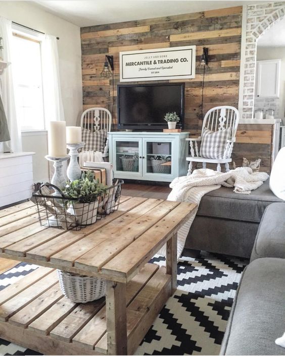 a rustic living room with a reclaimed wood wall, a wooden table, grey and blue furniture and refined vintage chairs