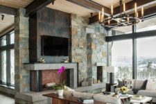 a rustic living room with a stone clad fireplace, dark metal and cocnrete, a wooden ceiling with beams and a wooden storage unit