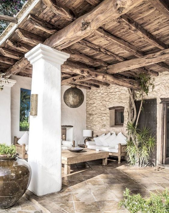 a rustic patio with white plaster, a stone wall, a wooden ceiling with beams and low wooden furniture