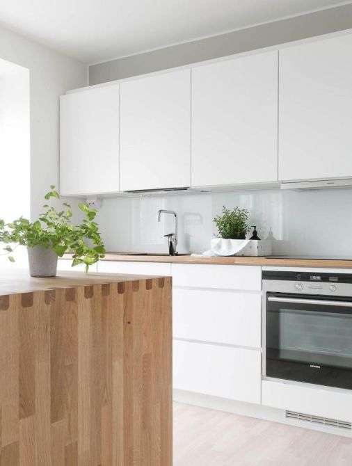 a sleek Nordic kitchen with white cabinets, a blue glass backsplash, a light stained wood kitchen island