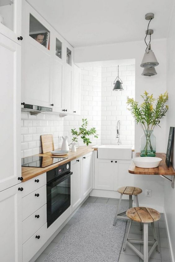 a small Nordic kitchen with white cabinets, black hardware, butcherblock countertops and white tiles plus wood and metal stools