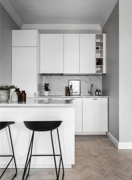 a small Nordic kitchen with white sleek cabinets and a grey stone countertop and blacksplash plus black stools