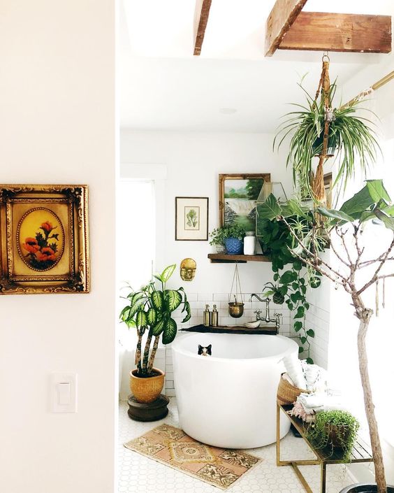 a small boho bathroom with a soak tub, a boho rug, potted greenery and artworks