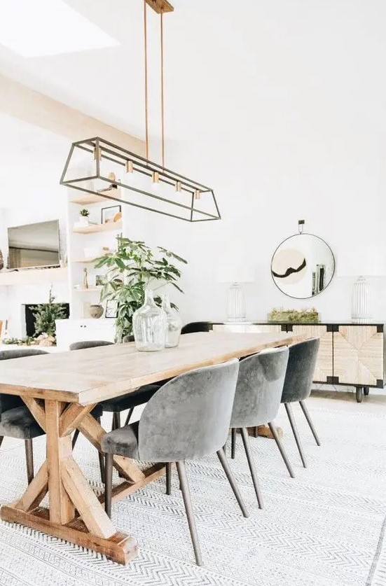 a stylish modern country dining room with a trestl table, grey chairs, a metal chandelier, an inlaid console and a round mirror