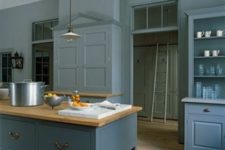 a vintage blue kitchen with paneled cabinets, wooden countertops and pendant lamps