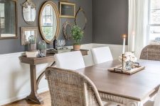a vintage farmhouse dining area with wicker and upholstered chairs, a wooden table and a gallery wall with frames and mirrors