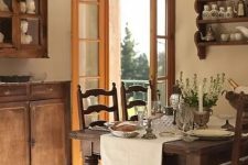 a vintage farmhouse dining room with stained furniture – a dining set, a wall-mounted shelf and some cabinets, a crystal chandelier