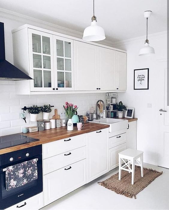 a white Scandi kitchen with vintage-inspired cabinets and black hardware, butcherblock countertops and pendant lamps