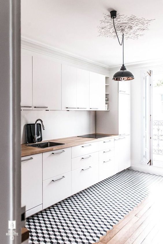 an airy Scandinavian kitchen with white cabinets, butcherblock countertops, a geometric floor and pendant lamps