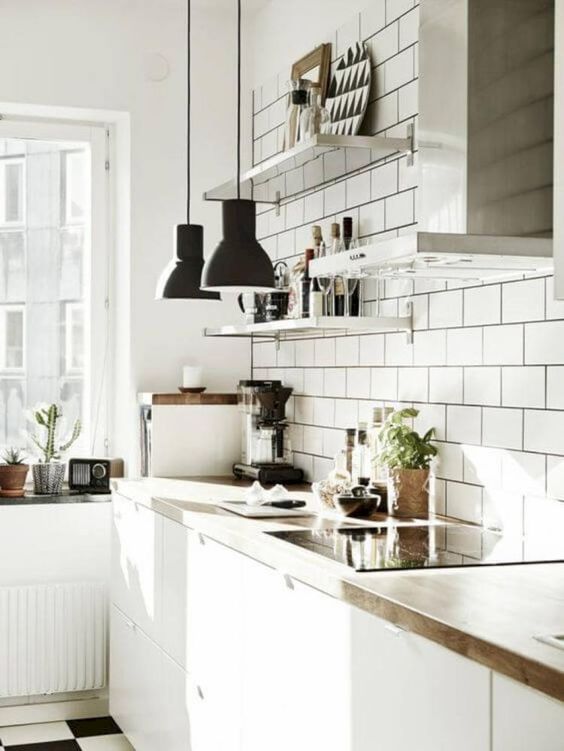 an airy kitchen with white tiles, white cabinets, wooden countertops, black pendant lamps