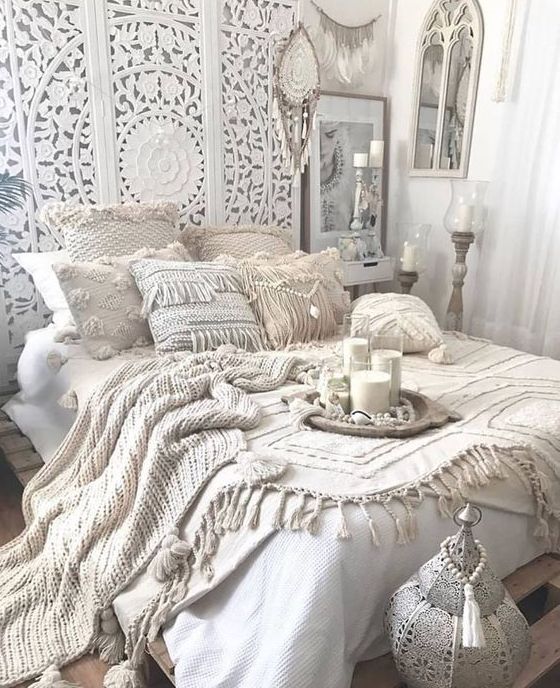 an all-white Moroccan bedroom with an ornate wodoen screen, crochet pillows and blankets, candles and lanterns and dream catchers