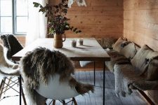 an eclectic chalet dining room with a corner bench with faux fur and pillows, a modern table and chair with fur