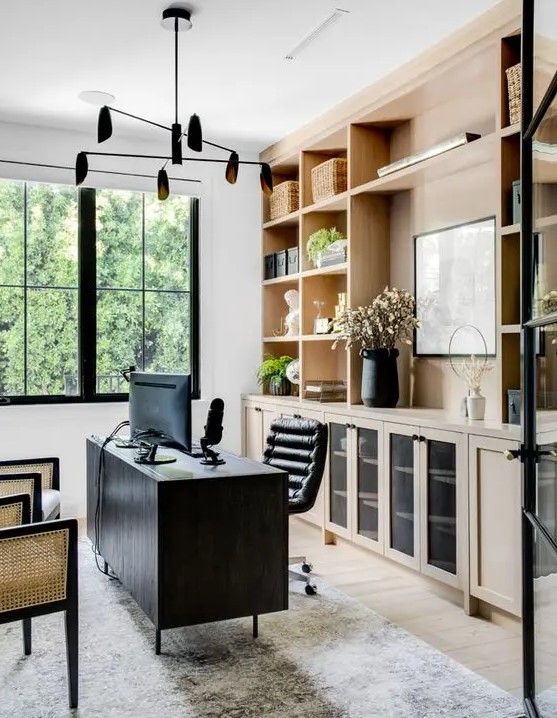 a beautiful and contrasting home office with light-stained cabinetry, a black desk and a chair, cane chairs and a black chandelier