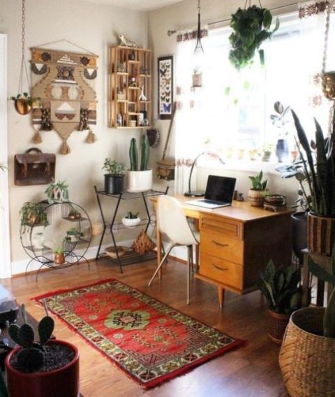 a boho chic home office with a retro wooden desk, a boho rug, a folksy artwork o the wall, lots of potted plants, cacti and succulents
