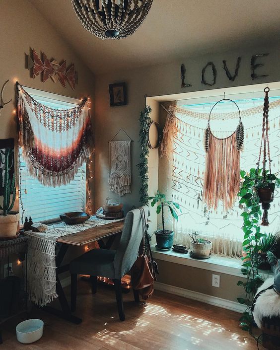 a boho chic home office with fringe and macrame hangings, potted plants, faux fur, a beaded chandelier and a macrame runner on the desk