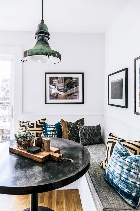 a boho dining nook with printed pillows, a black round table and a metal pendant lamp