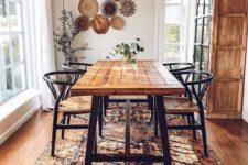 a boho dining room with a beautiful Eastern rug, an arrangement of decorative plates, a wooden table and wicker chairs