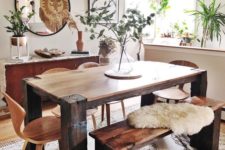a boho dining space with a wooden set, a mid-century modern chandelier, a round mirror and greenery arrangements