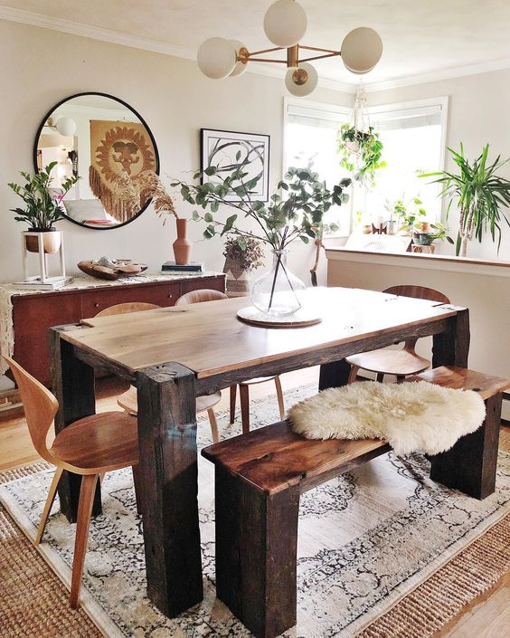 a boho dining space with a wooden set, a mid-century modern chandelier, a round mirror and greenery arrangements
