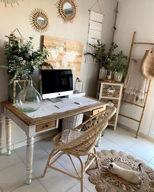 a boho eclectic home office with a vintage desk, a rattan chair, a jute rug, a ladder, sunburst mirrors, a lot of greenery and a map