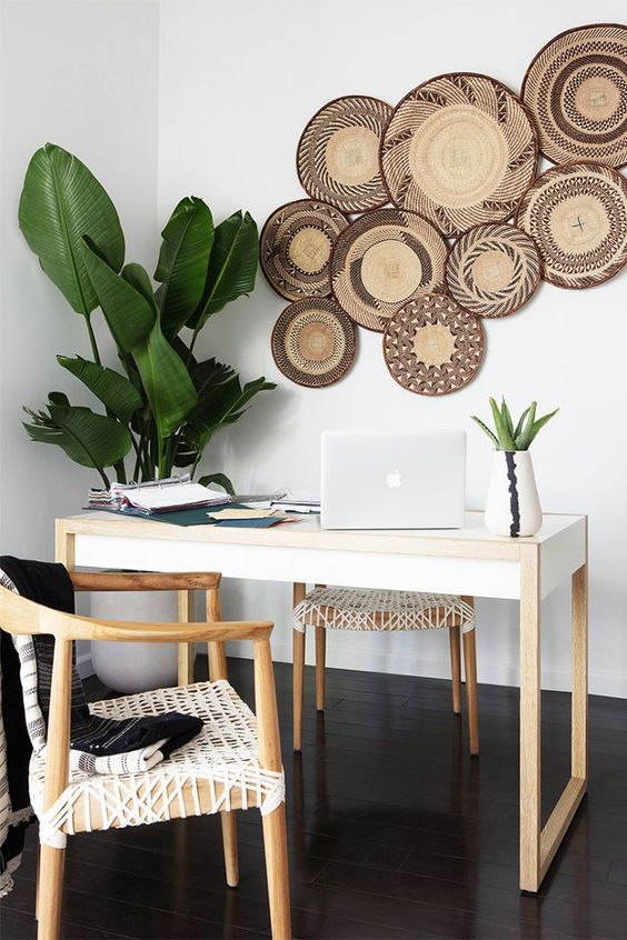 a boho tropical home office with a sleek desk, woven chairs, potted plants, decorative plates on the wall is very airy and cool