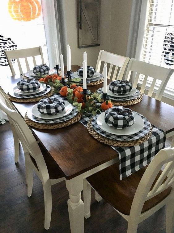 a bold farmhouse tablescape with plaid runner, chargers and fabric pumpkins, woven placemats and a bright pumpkin centerpiece