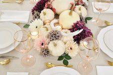 a bright and chic fall centerpiece of white and purple blooms, antlers, candles and foliage plus white pumpkins