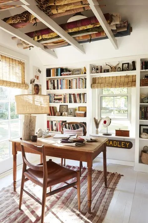 a catchy farmhouse home office with built-in storage units and shelves, a wooden desk and chair, a rustic lamp and woven shades