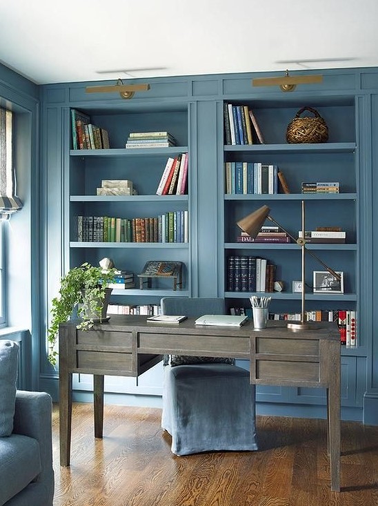 a chic blue home office with built-in storage units, a weathered wooden desk, gold and brass touches