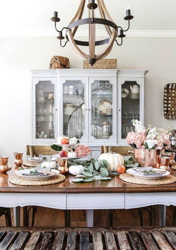 a chic fall tablescape with neutral pumpkins, apples, greenery, woven placemats, a copper pot with blooms