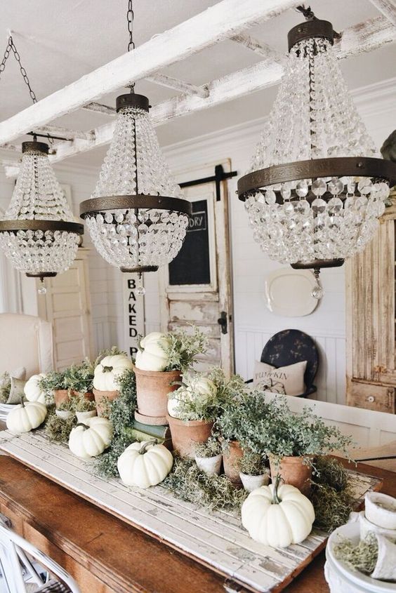a chic neutral farmhouse centerpiece of a wooden board with greenery, neutral pumpkins and pots