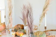 a classy fall centerpiece of gilded pumpkins and spray painted pampas grass plus candles for a modern table setting