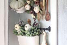 a colander with a green pumpkin, a wreath with leaves, pinecones and pumpkins and a pot with greenery and white pumpkins