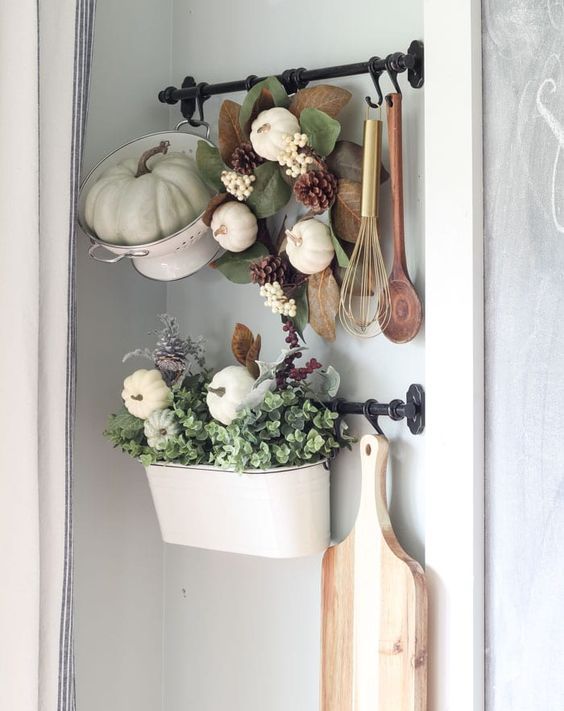 une passoire avec une citrouille verte, une couronne avec des feuilles, des pommes de pin et des citrouilles et un pot avec de la verdure et des citrouilles blanches une passoire avec une citrouille verte, une couronne avec des feuilles, des pommes de pin et des citrouilles et un pot avec de la verdure et des citrouilles blanches