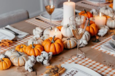 a colorful fall table with plaid placemats, bright pumpkins and cotton, pillar candles and fall leaves instead of place cards